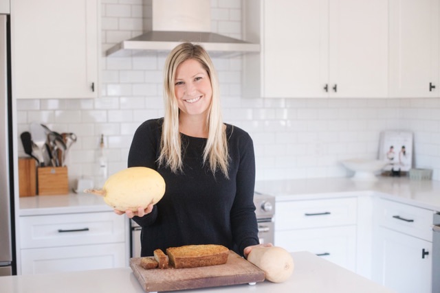 Woman in her kitchen with freshly baked bread and squash from the garden on the counter.