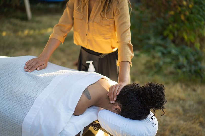 patient on a massage table lying facedown while the practitioner puts her hands on the back of neck and lower body on the patient.